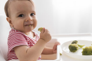 Bébé qui mange tout seul des brocolis.