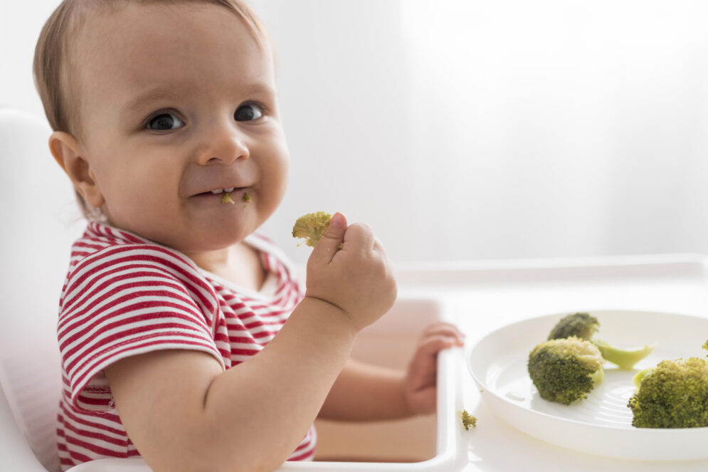 Bébé qui mange tout seul des brocolis.