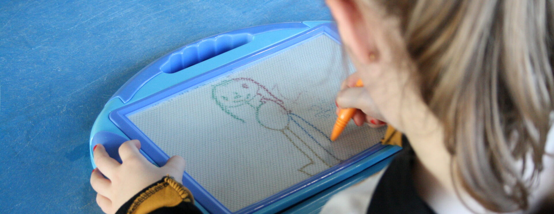 Fillette vue de dos qui dessine sur une ardoise magique lors des ateliers de la Maison des Enfants du Pays de l'Ourcq à Ocquerre