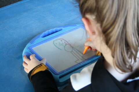 Fillette vue de dos qui dessine sur une ardoise magique lors des ateliers de la Maison des Enfants du Pays de l'Ourcq à Ocquerre